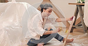 Young brunette female artist with inspiration draws a picture on canvas in an art studio, sitting on the floor.