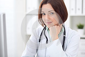 Young brunette female doctor sitting at a desk and working on the computer at the hospital office.