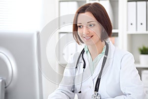 Young brunette female doctor sitting at a desk and working on the computer at the hospital office.