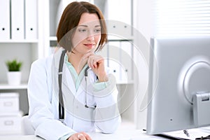 Young brunette female doctor sitting at the table and working at hospital office.