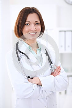 Young brunette female doctor standing with arms crossed and smiling at hospital