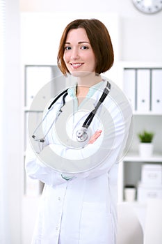 Young brunette female doctor standing with arms crossed and smiling at hospital