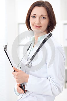 Young brunette female doctor standing with clipboard and smiling at hospital.