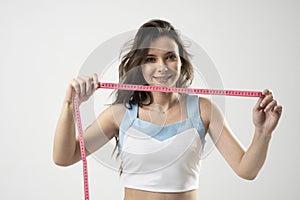 Young brunette fitness woman with pink measure tape before measuring her waistline on white background. Time for diet