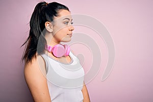 Young brunette fitness woman wearing gym headphones over pink isolated background looking to side, relax profile pose with natural