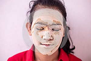 Young brunette girl with ayurvedic natural hearbal cosmetic facial mask applied over her face. multani mitti / fuller earth clay
