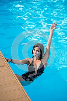 Young brunette girl with a beautiful smile in a swimming pool holding on to a broadside of pool