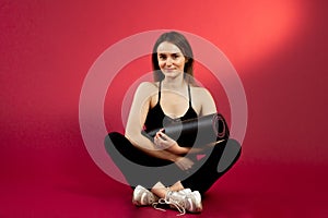 Young brunette girl in a black top crossing her legs. A sports woman on a red cherry background