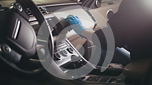 Young brunette girl in gloves is washing with brush a car dashboard and steering wheel