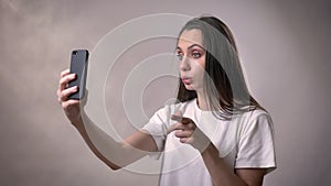 Young brunette girl has a video call on smartphone, communication concept, grey background