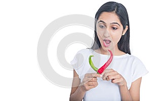 Young brunette girl holding red and green pepper chilli with surprised expression on her face isolated on white background