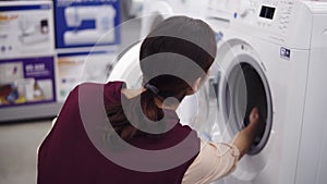 Young brunette girl opens a washing mashine door, spins the cylinder inside and pulls out detergent tray. Costumer