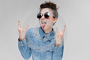 Young brunette girl in round glasses. Hairs are gathered in a bun. The girl shows a rocker goat.