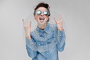 Young brunette girl in round glasses. Hairs are gathered in a bun. The girl shows a rocker goat.