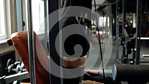 Young brunette girl is sitting on the simulator getting ready for an exercise in the gym