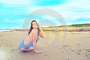 Young brunette girl in striped swimsuit sitting on the beach on the sand Shining bright sun blue sky clouds