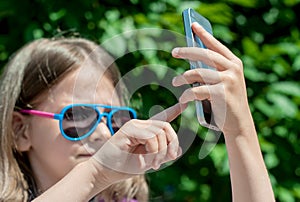 Young brunette girl in summer day walking, enjoying the sun and making selfie portrait. A sweet baby holds a mobile phone in hands