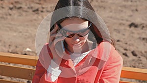 Young brunette girl in sunglasses waiting for a call on the phone sitting in the Park on the bench.