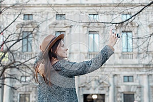 A young brunette girl takes pictures holding a hat with her hand