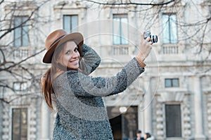 A young brunette girl takes pictures holding a hat with her hand and looks directly into the frame