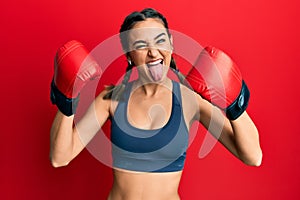Young brunette girl using boxing gloves wearing braids sticking tongue out happy with funny expression