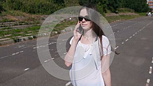 Young brunette girl walking in the stadium, dials a number on mobile phone and waiting for an answer.