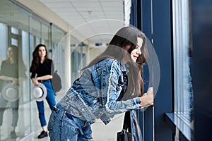 Young brunette girl, wearing casual jeans clothes, leaning on railing in light airport hallway with huge windows, with her