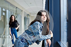 Young brunette girl, wearing casual jeans clothes, leaning on railing in light airport hallway with huge windows, with her