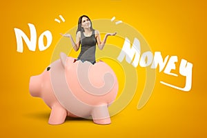 Young brunette girl wearing casual jeans and t-shirt appearing out of broken piggy bank with NO MONEY sign on yellow