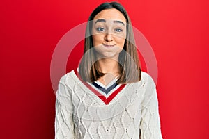Young brunette girl wearing casual student sweater puffing cheeks with funny face