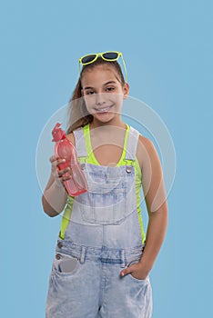 Young brunette girl wearing  denim overalls shorts stands with a phone and with a bottle of water