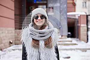 Young brunette girl,wearing grey fur coat, knit hat and sunglasses,walking from outside coffee shop,smiling laughing. Winter
