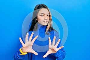 Young brunette girl wearing turtleneck sweater afraid and terrified with fear expression stop gesture with hands, shouting in