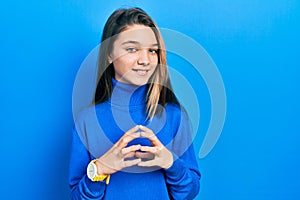 Young brunette girl wearing turtleneck sweater hands together and fingers crossed smiling relaxed and cheerful