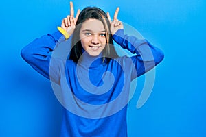 Young brunette girl wearing turtleneck sweater posing funny and crazy with fingers on head as bunny ears, smiling cheerful