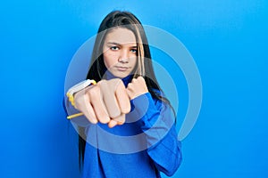 Young brunette girl wearing turtleneck sweater punching fist to fight, aggressive and angry attack, threat and violence