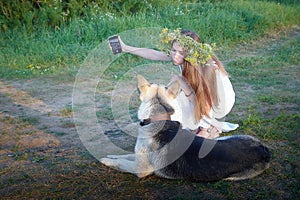 Young brunette girl in a white dress, sundress and a wreath of flowers with big shepherd dog in summer on the coast of