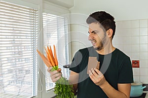 A young brunette man looks at a carrot with disdain and disgust. photo