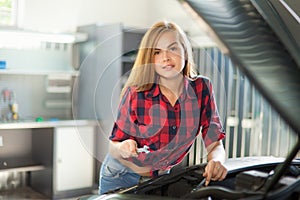 Young brunette mechanic in checked shirt in garage.