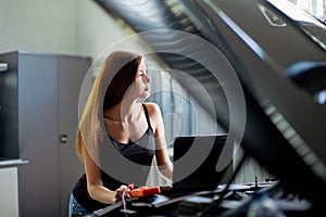 Young brunette mechanic in checked shirt in garage. Auto di