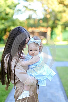 Young brunette mother holding little female baby in garden.