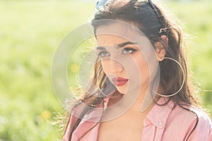 Young brunette with perfect make-up, trendy sunglasses enjoying sunny day in park or garden. Attractive girl with big