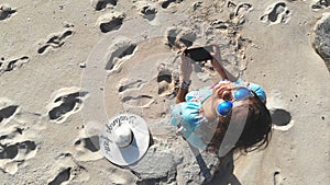 Young brunette pretty woman controls piloting drone copter using console holding phone at ocean beach. Smart girl