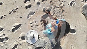 Young brunette pretty woman controls piloting drone copter using console holding phone at ocean beach. Smart girl