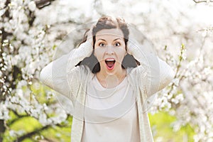 Young brunette shocked beautiful woman in light casual clothes screaming clinging to head closing ears standing in city