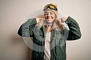 Young brunette skier woman wearing snow clothes and ski goggles over white background smiling cheerful showing and pointing with
