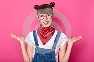 Young brunette student in confusion, stand with open mouth isolated over pink background. Schoolgirl with two funny bunches, wears