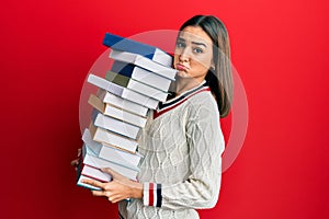 Young brunette student girl holding a pile of books depressed and worry for distress, crying angry and afraid