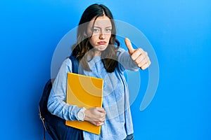 Young brunette student woman wearing student backpack doing thumbs up gesture depressed and worry for distress, crying angry and