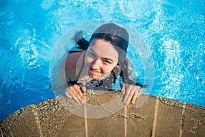 Young brunette teen girl posing in a blue swimming pool in a hotel in Turkey